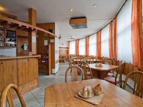 Sál restaurace V Oblouku — dřevěný barový pult, stoly se židlemi a okna s oranžovými závěsy