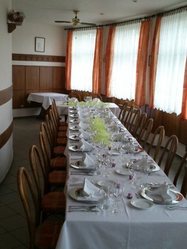 Dlouhá slavnostní tabule s bílým ubrusem, sklem a zelenou dekorací